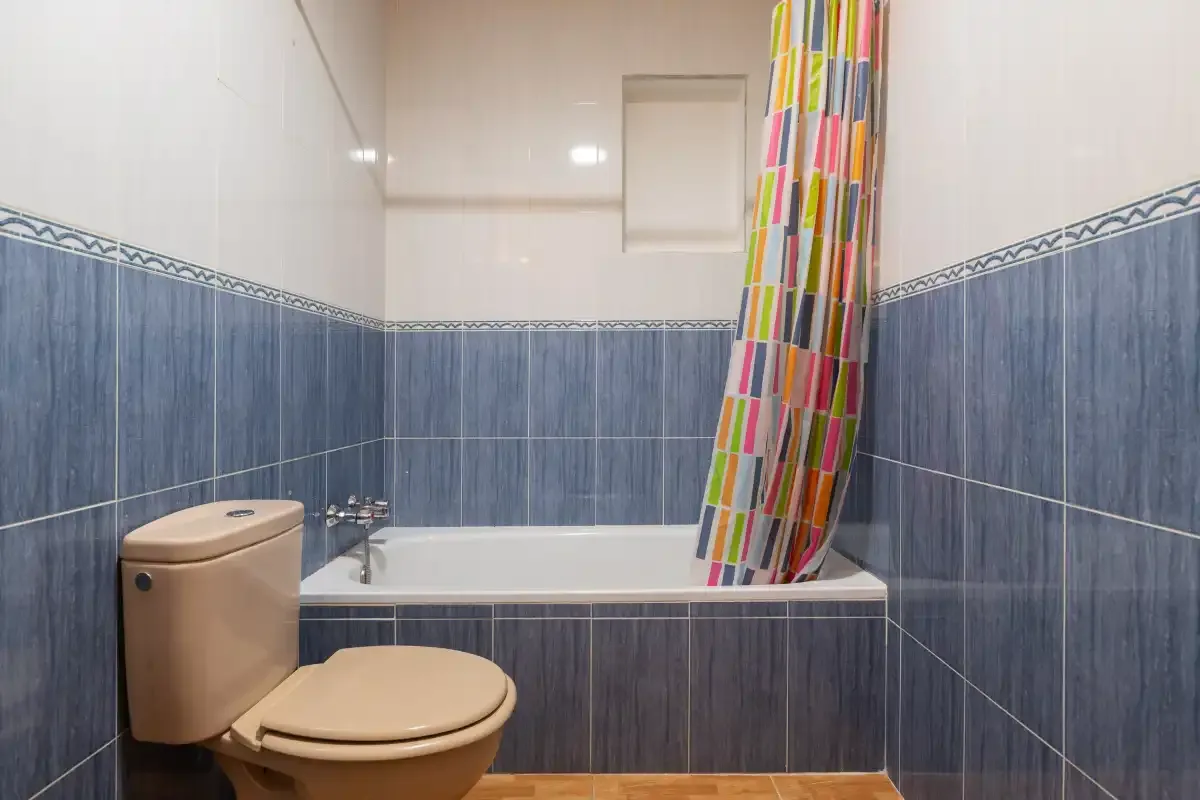 Baño alicatado con bañera, inodoro y cortina de ducha de colores.