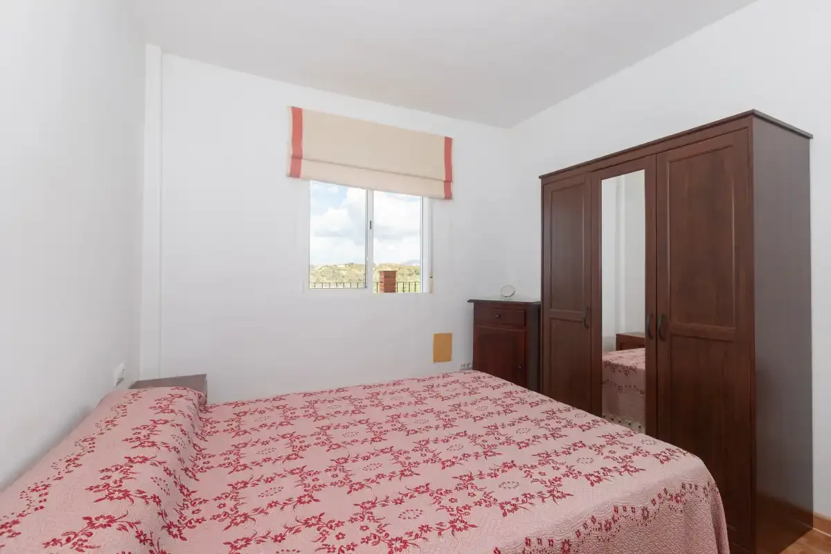 Un dormitorio con una cama cubierta con una colcha rosa de flores y un armario de madera.