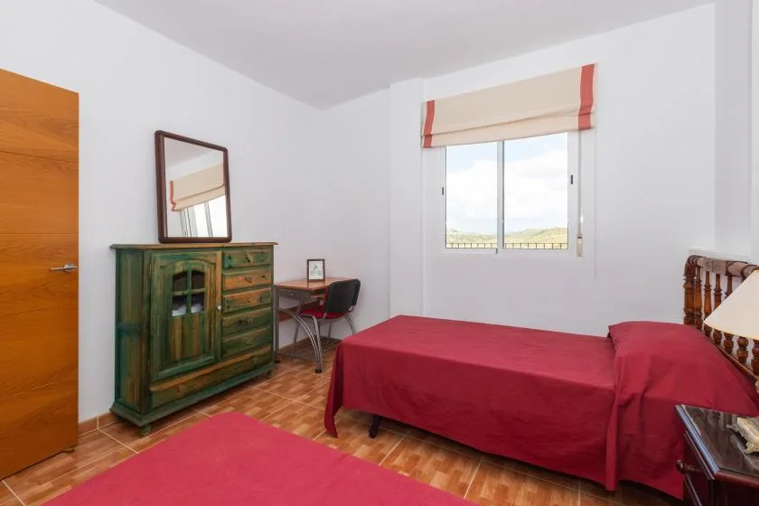 Un dormitorio con camas cubiertas de rojo, una cómoda de madera y una ventana.