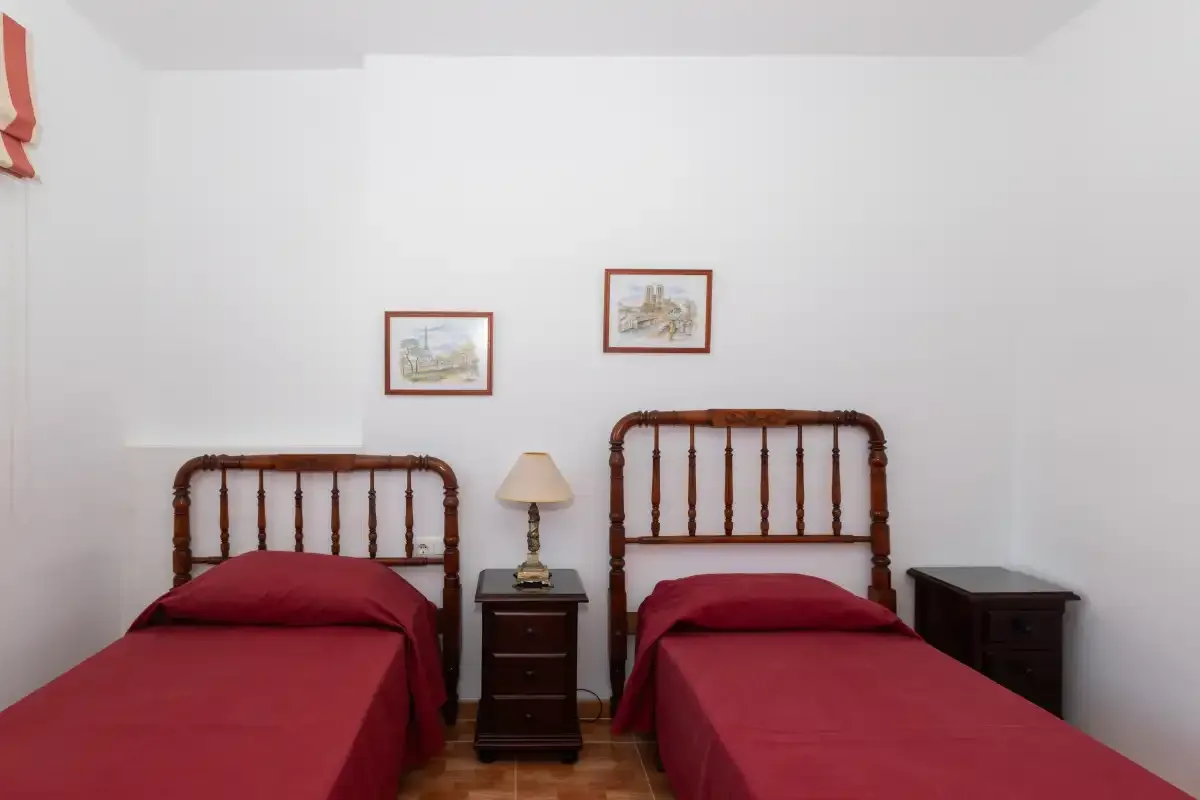 Un dormitorio con dos camas vestidas de rojo y pequeños cuadros en la pared.