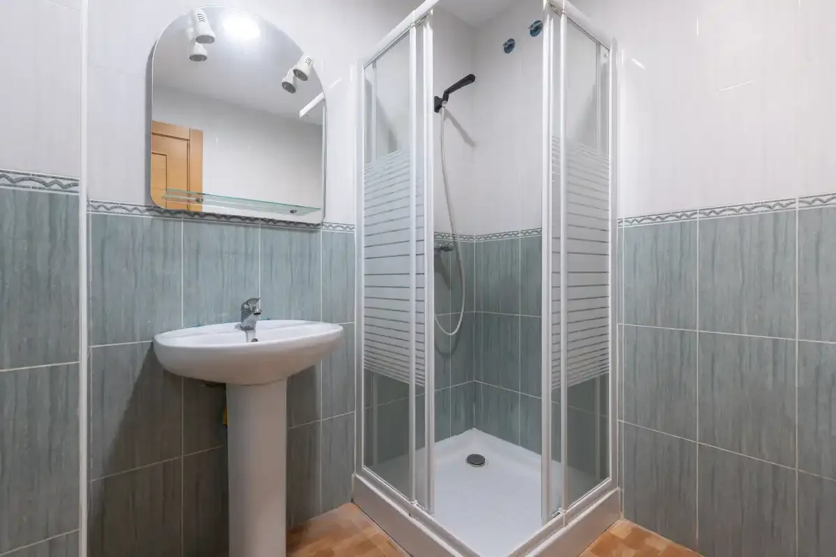 Un baño alicatado con lavabo de pedestal y ducha.