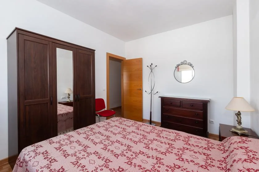 Un dormitorio con una colcha estampada, un armario oscuro y una cómoda.