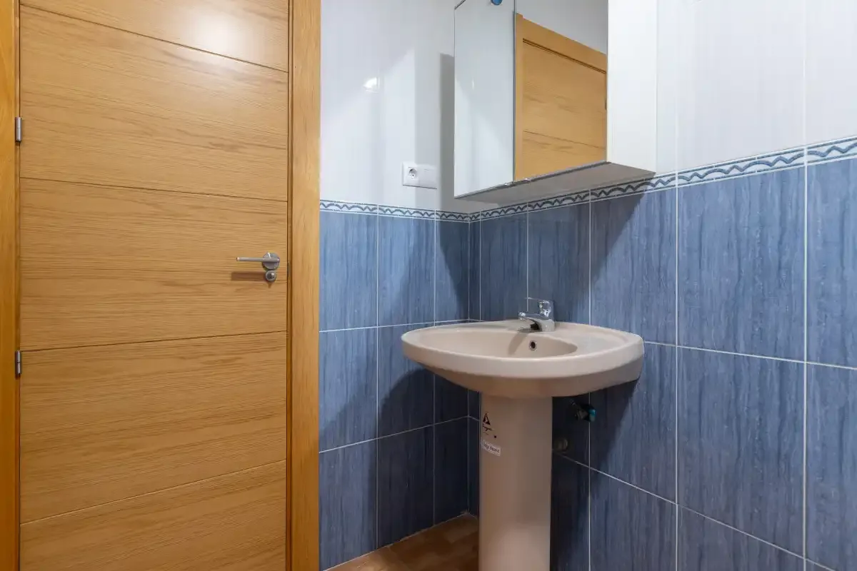 Un baño con lavabo de pedestal, espejo y puerta de madera.