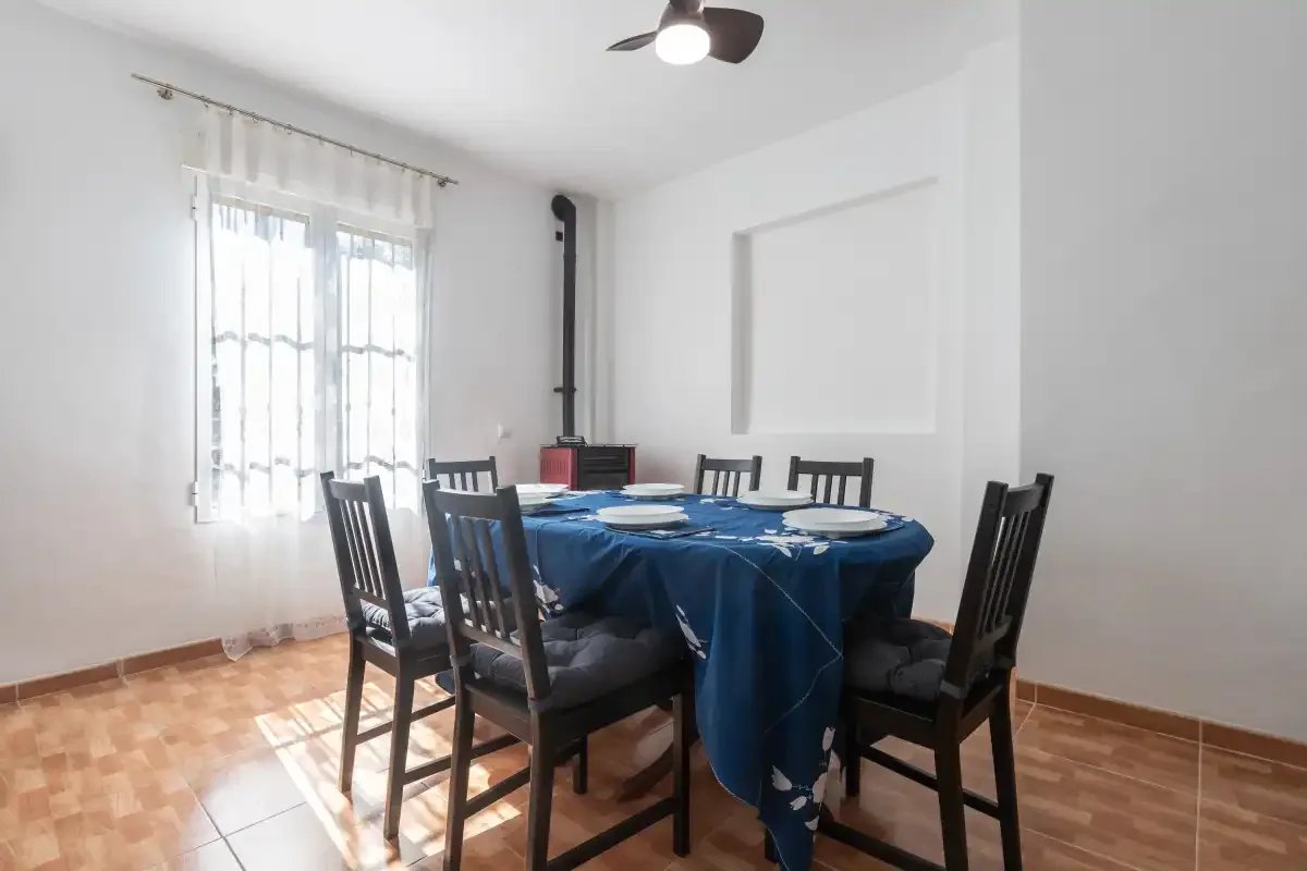 Un comedor con una mesa cubierta con un mantel azul y asientos oscuros.