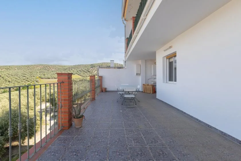 Una amplia terraza exterior con asientos de patio tiene vistas a una colina verde.