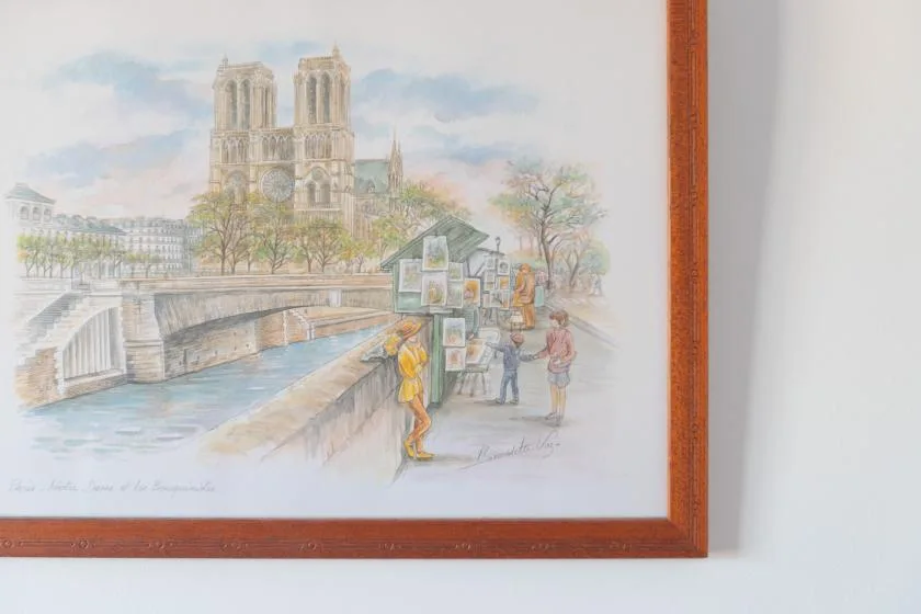 Una acuarela enmarcada muestra un puente junto al río, árboles y torres de una catedral.