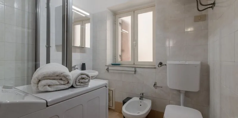 A tiled bathroom with a sink, toilet, and folded towels on the counter.