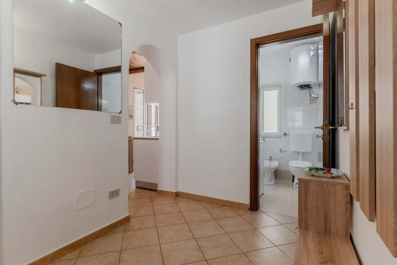 A tiled interior hallway opens onto a bathroom with a toilet and sink.