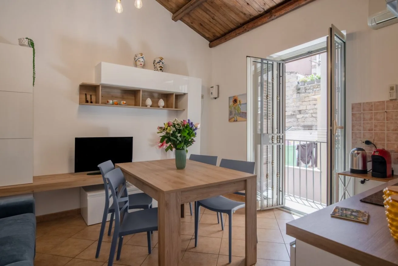 A dining area with a wooden table and chairs, beside an open balcony door.