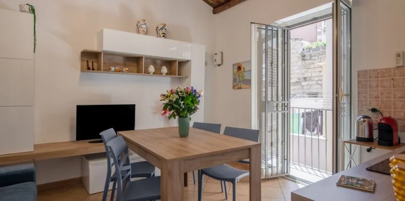 Un comedor con una mesa de madera, asientos y una puerta abierta al balcón.