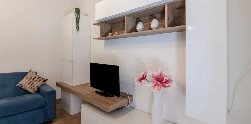 A living room with a television on a wooden shelf beside a blue sofa.
