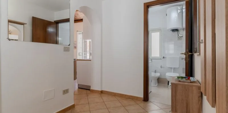 A tiled hallway opens onto a bathroom with a sink and toilet.