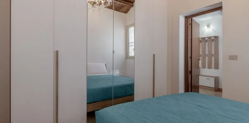 A bedroom with a teal bed beside mirrored wardrobe doors.