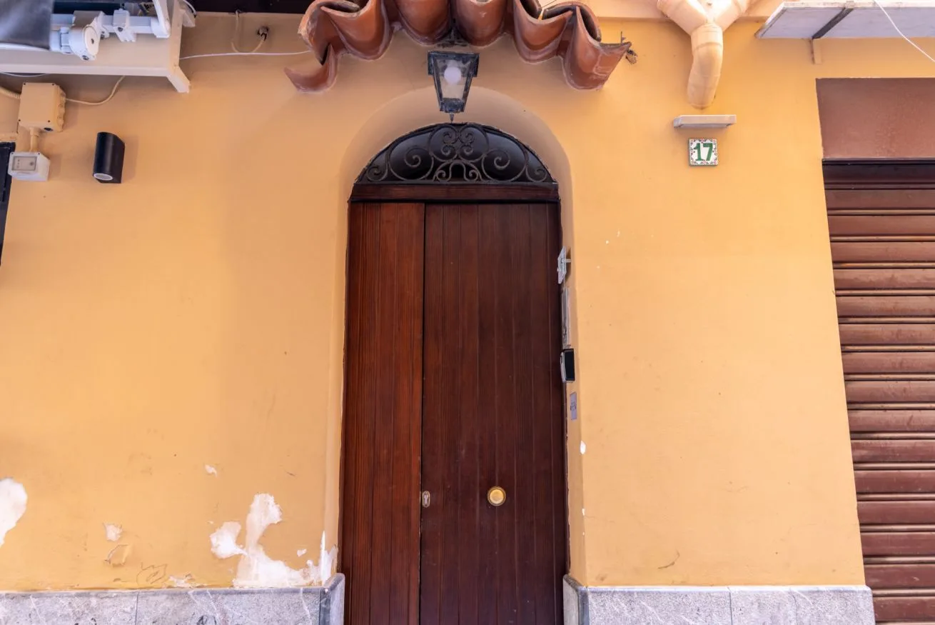 An arched wooden doorway with a decorative metal grille sits in a yellow wall.