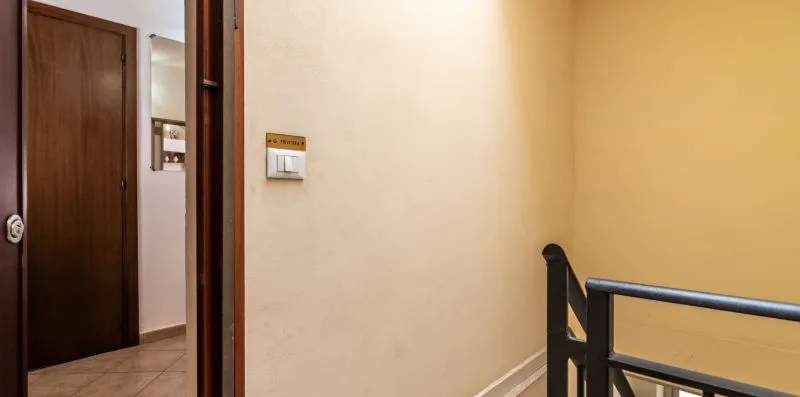 A hallway with a wooden door and a dark railing beside a pale wall.