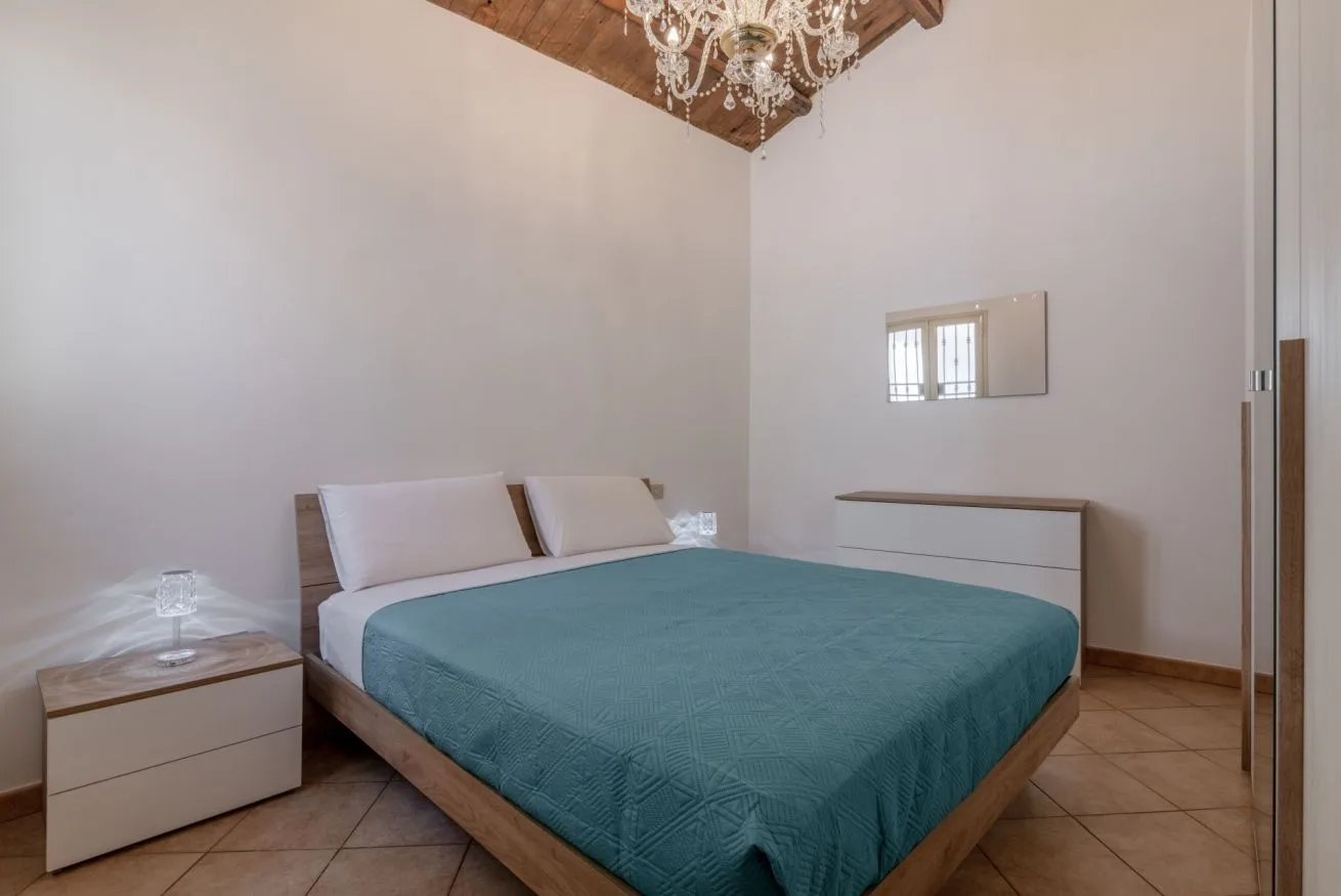 Bedroom with a bed covered in teal bedding and a chandelier overhead.