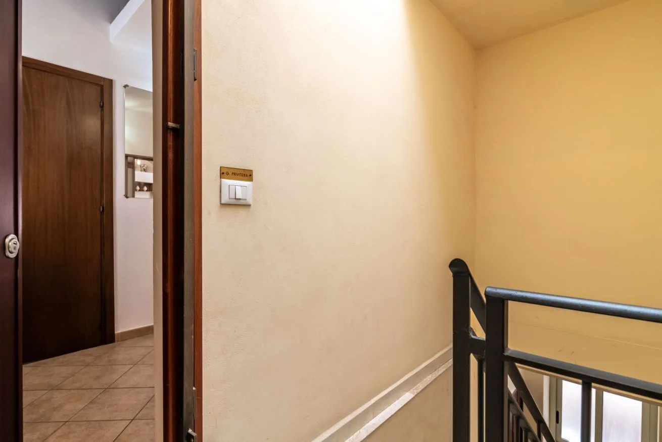 An indoor hallway with a wooden door and a dark railing.