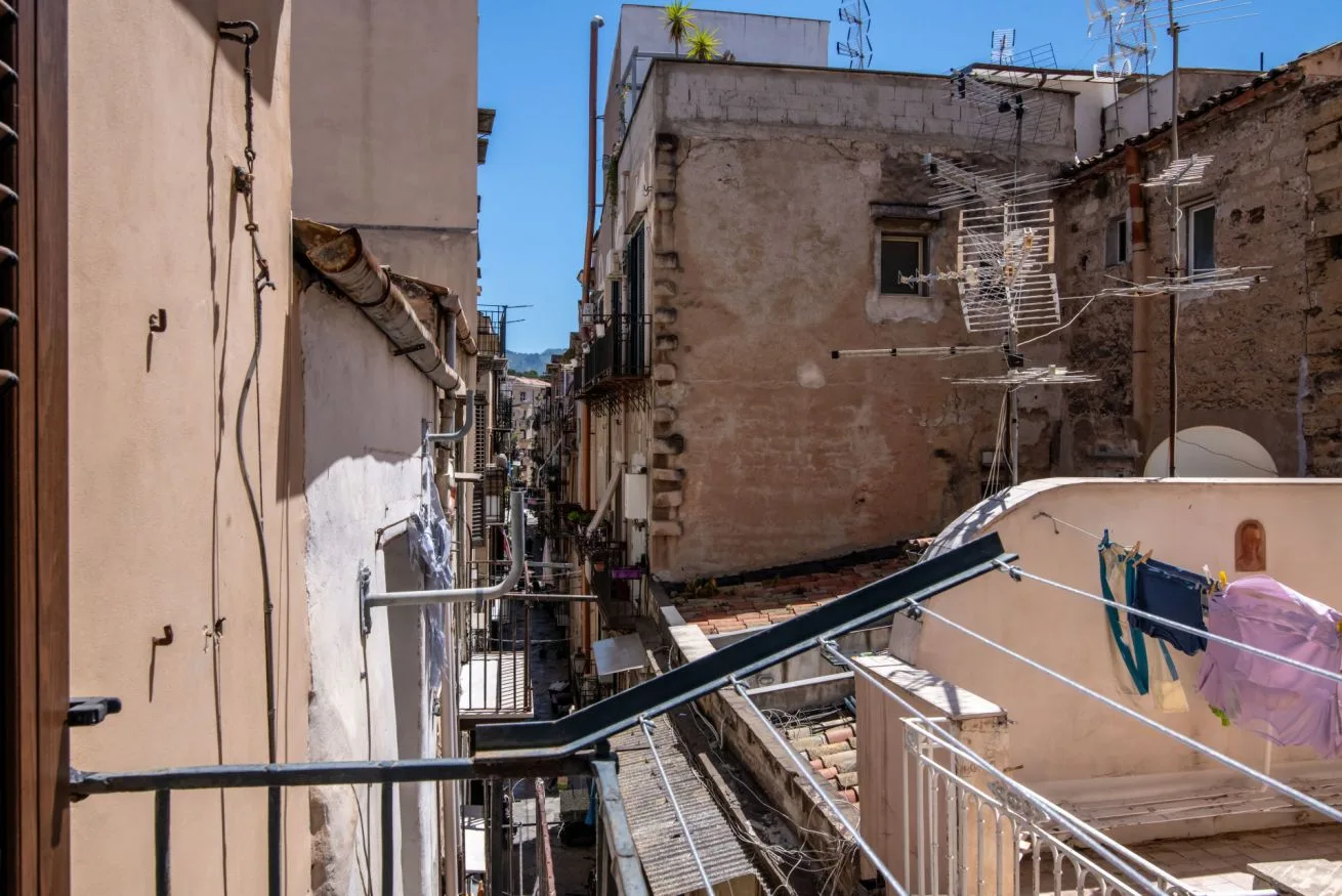 A narrow urban alley runs between closely spaced buildings beneath a clear blue sky.