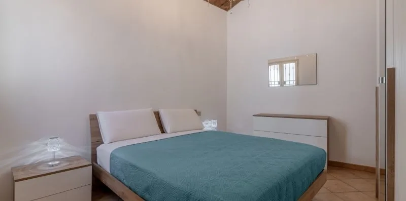 Un dormitorio con una cama cubierta con ropa de cama color turquesa y una ventana pequeña.