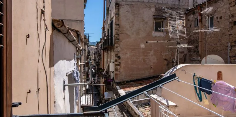 A narrow urban alley runs between closely spaced buildings, with laundry hanging overhead.