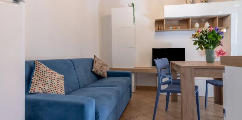 Una zona de estar y comedor con asientos azules, una mesa de madera y flores.