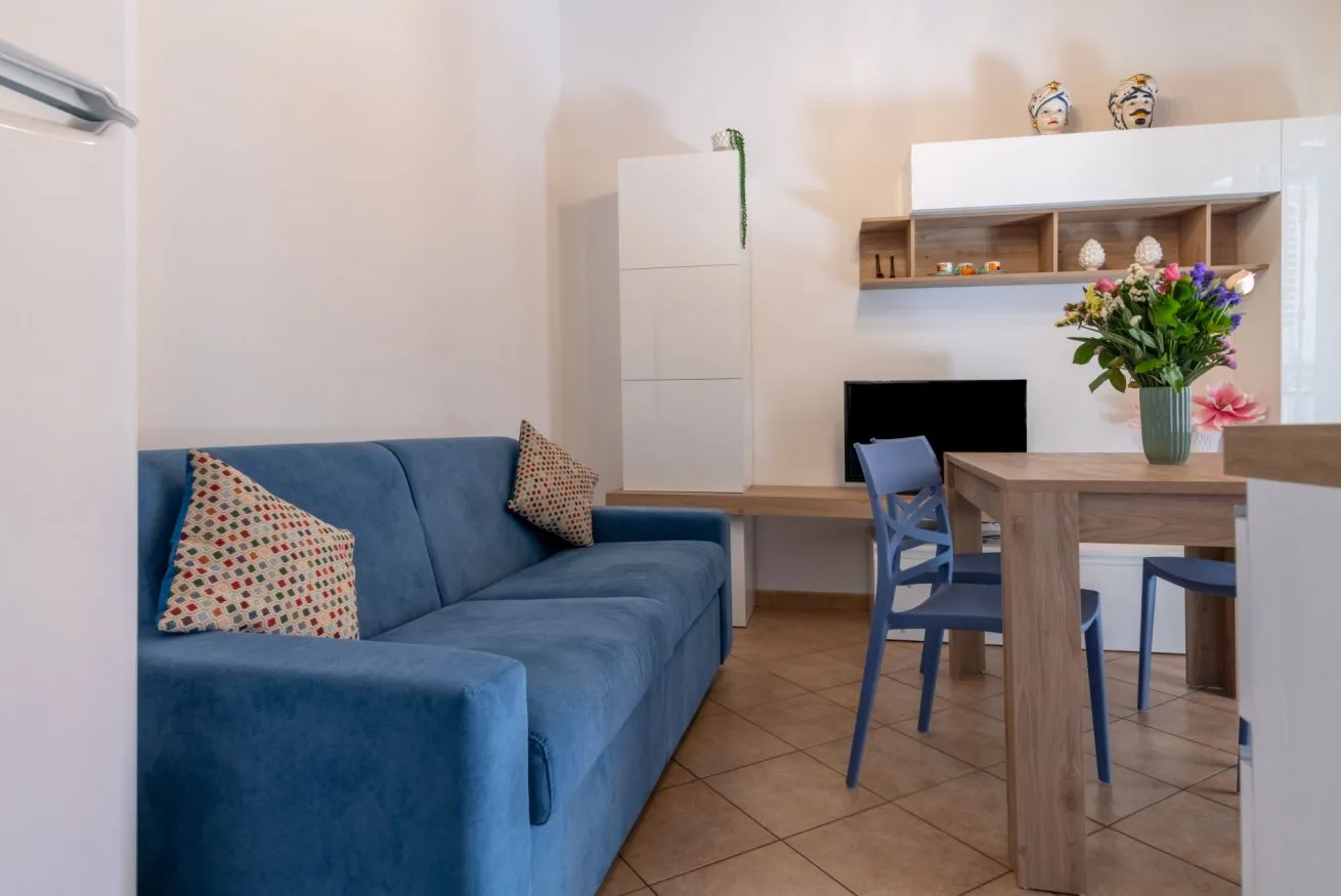 A living area with blue seating beside a dining table and flowers.