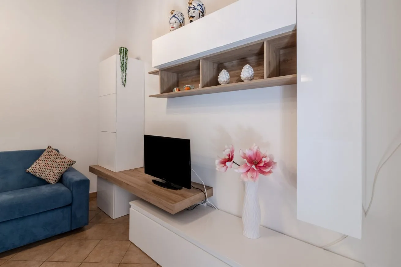 A living room with a television on a wooden media console and flowers nearby.