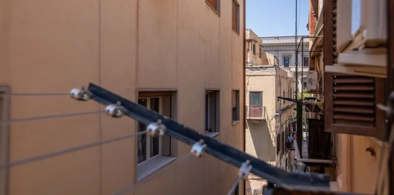 A narrow alley between closely spaced buildings, with balconies and overhead wires.