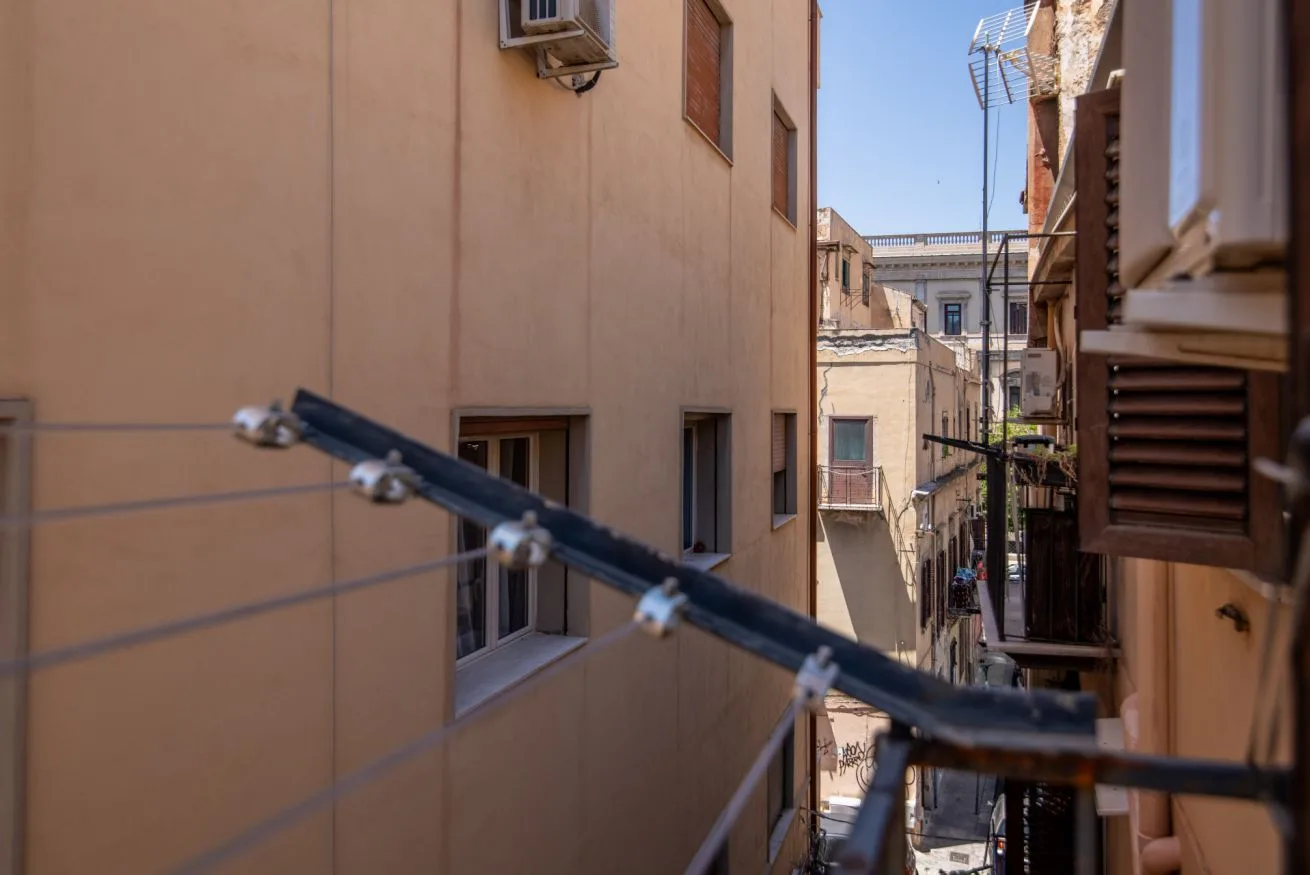 A narrow urban alley runs between closely spaced buildings, with windows and balconies.