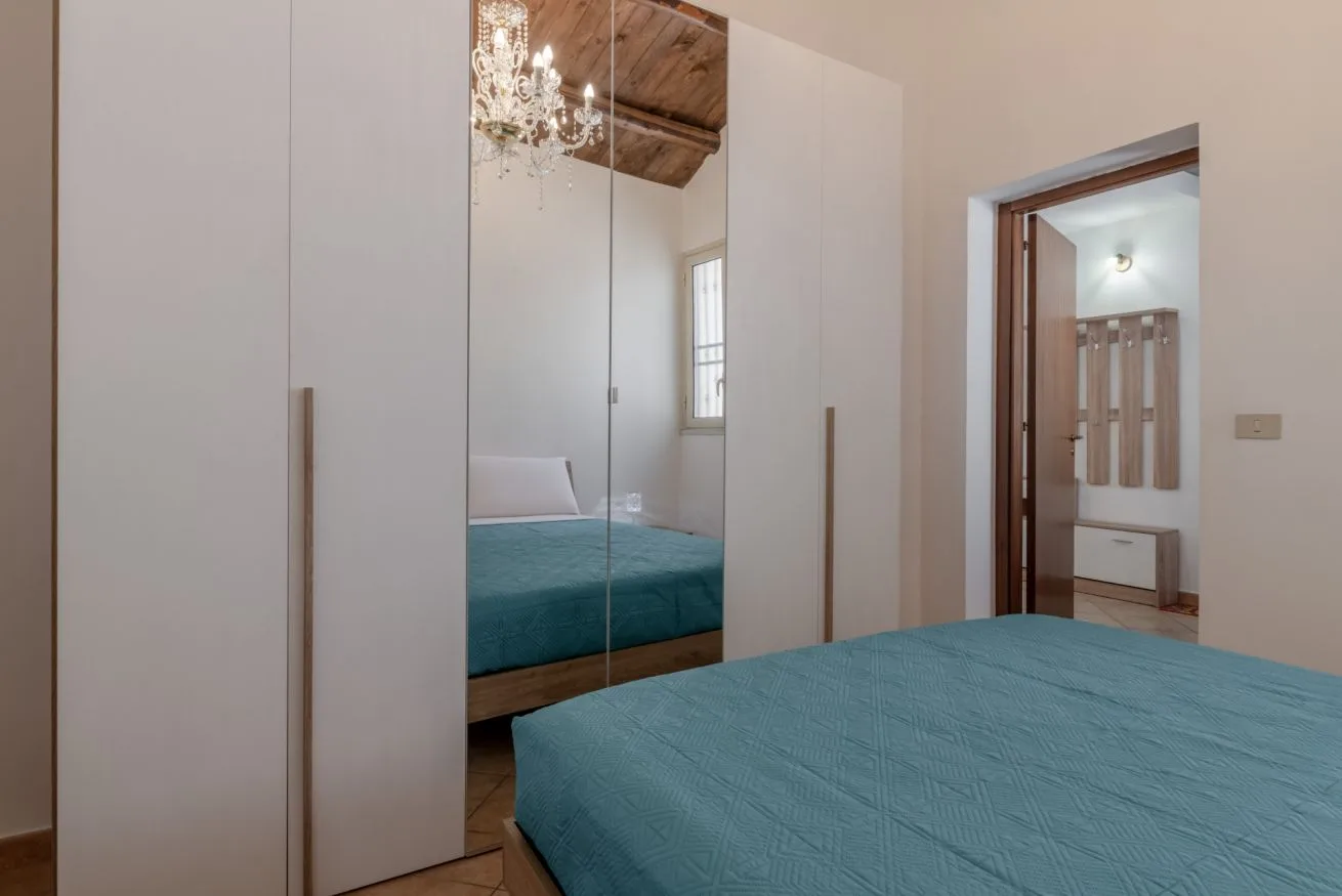 A bedroom with a teal bed beside mirrored wardrobe doors.