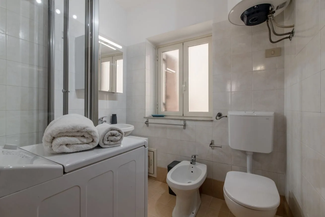 A tiled bathroom with a sink, bidet, toilet, and window.
