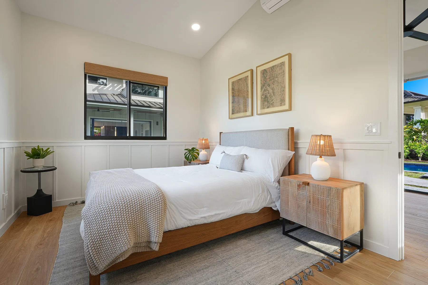 A bright bedroom with a neatly made bed and framed artwork above it.
