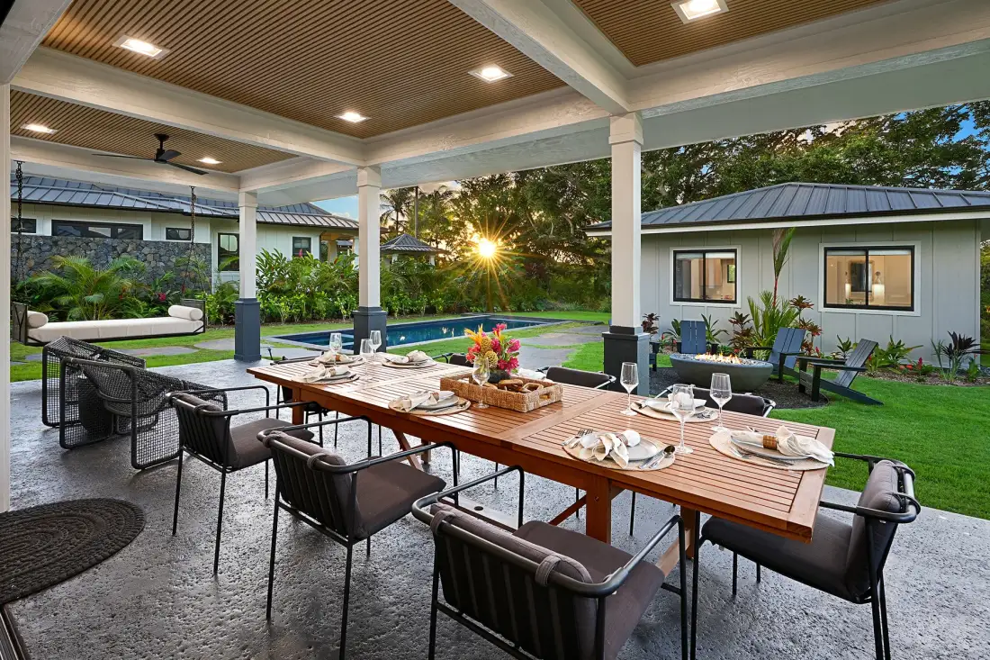 Una zona de comedor exterior cubierta da a una piscina y un jardín.