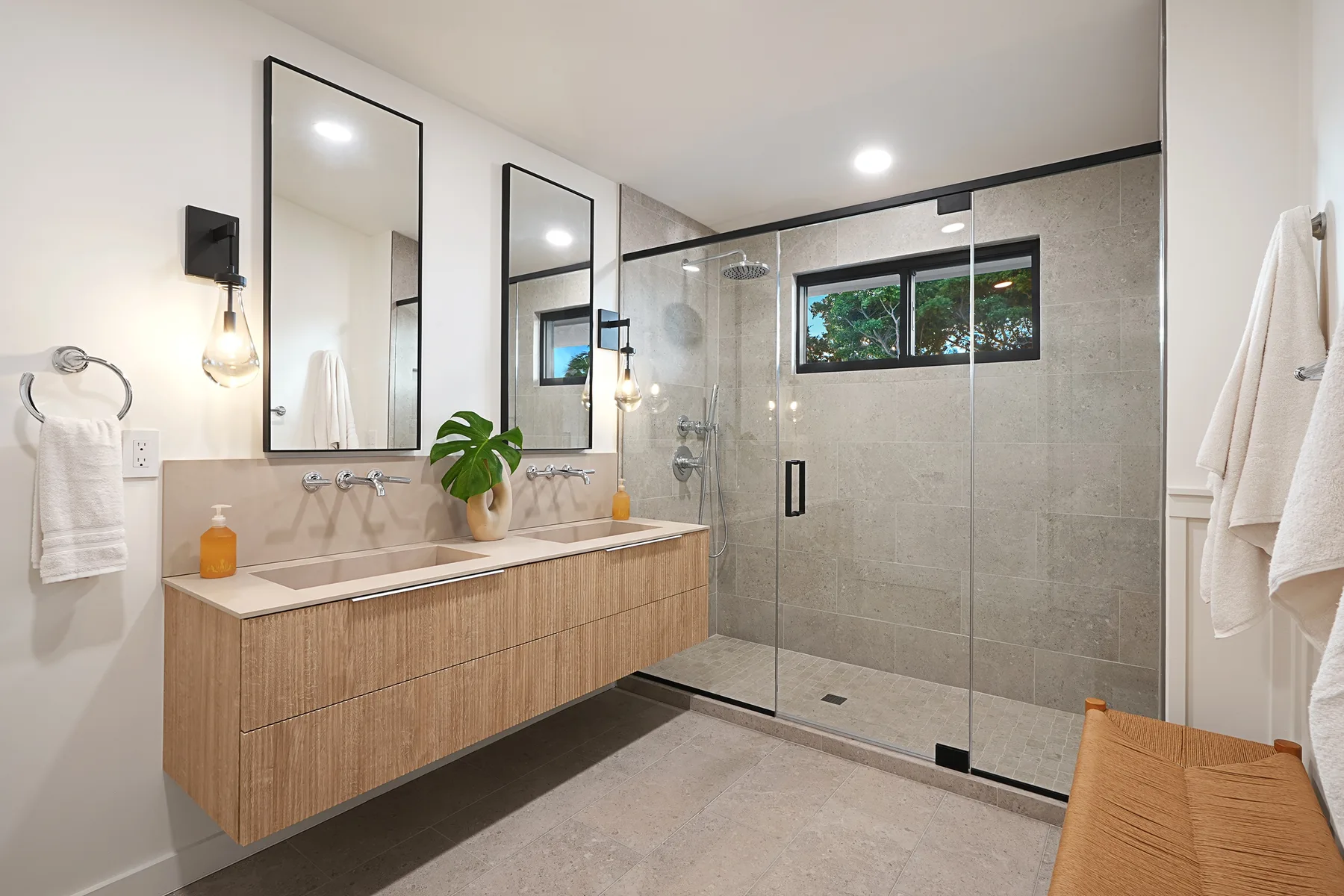 A bright bathroom with a long vanity and a glass-enclosed shower.