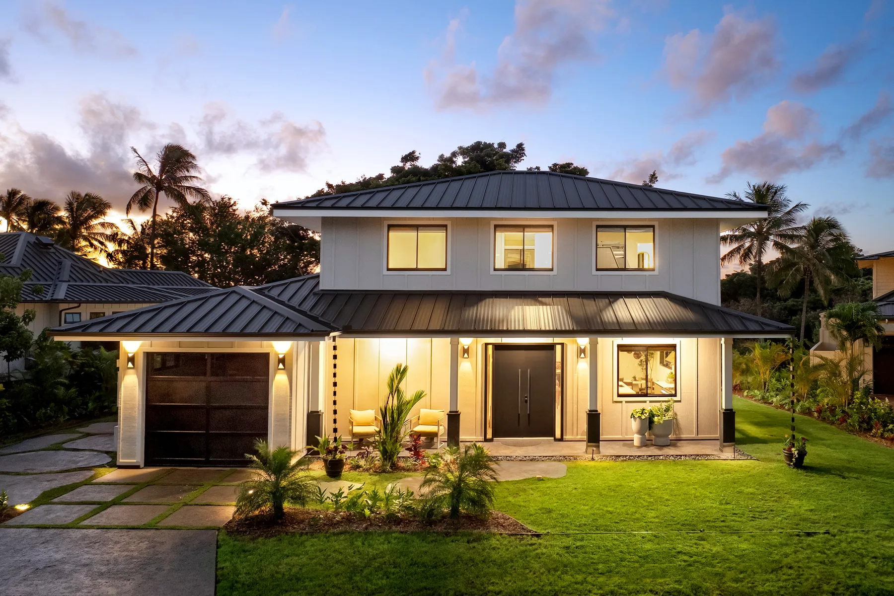 A two-story house with a driveway and lawn at dusk.