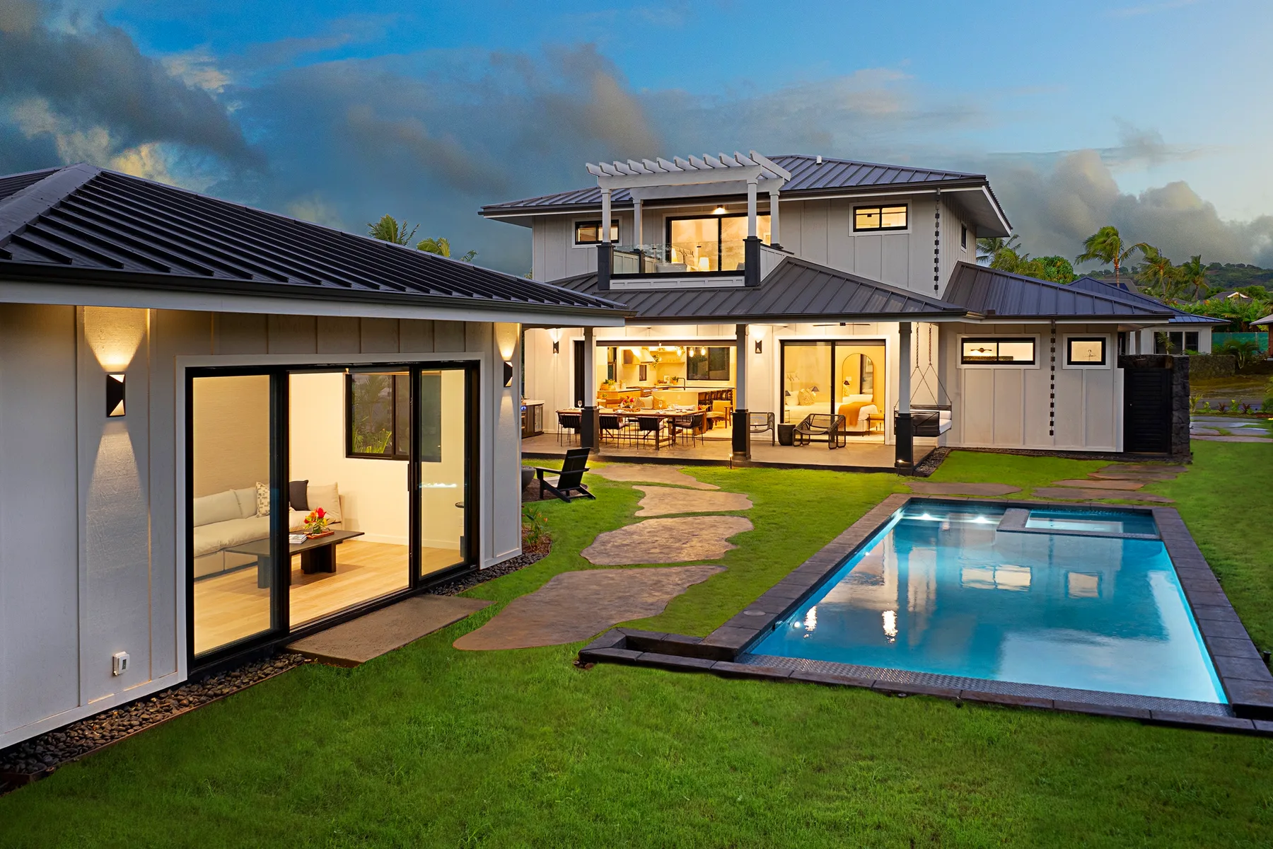 Casa moderna con césped, patio y piscina al anochecer.