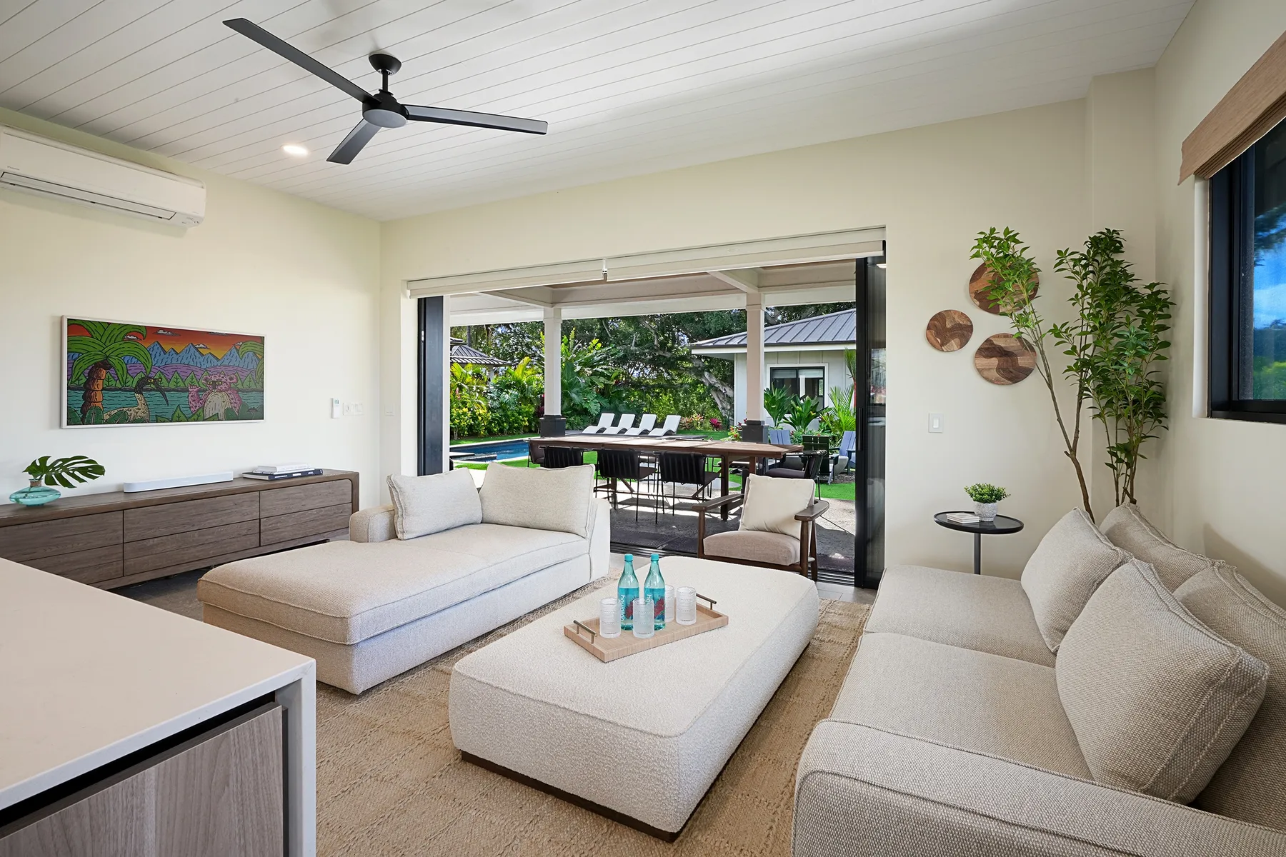 A bright living room opens onto an outdoor dining area, with light-colored seating.