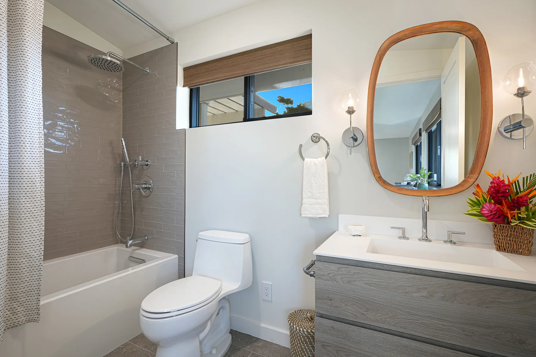 A bright bathroom with a bathtub, toilet, and vanity beneath a rounded mirror.