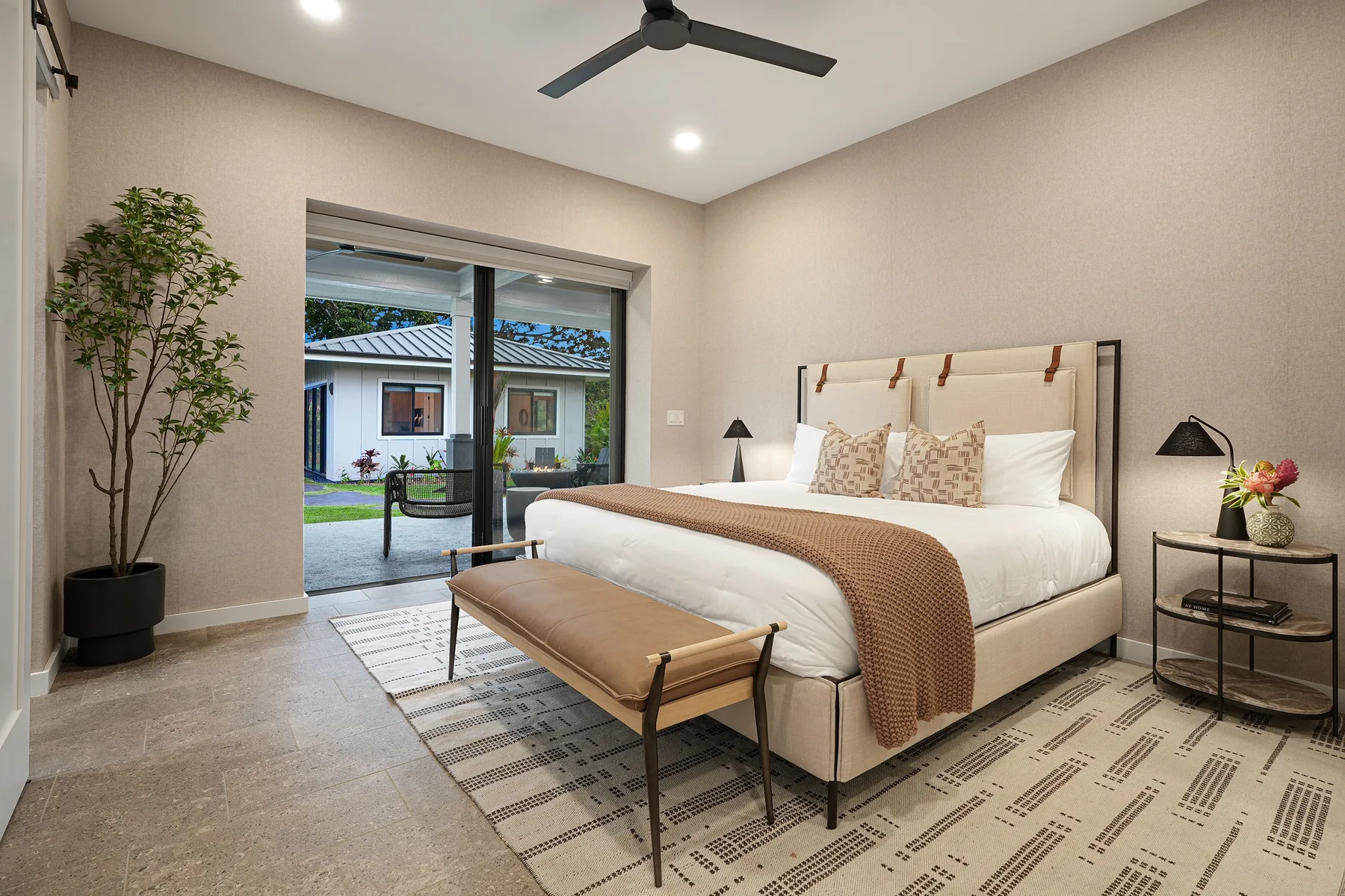 A bright bedroom with a large bed, a bench, and sliding glass doors.