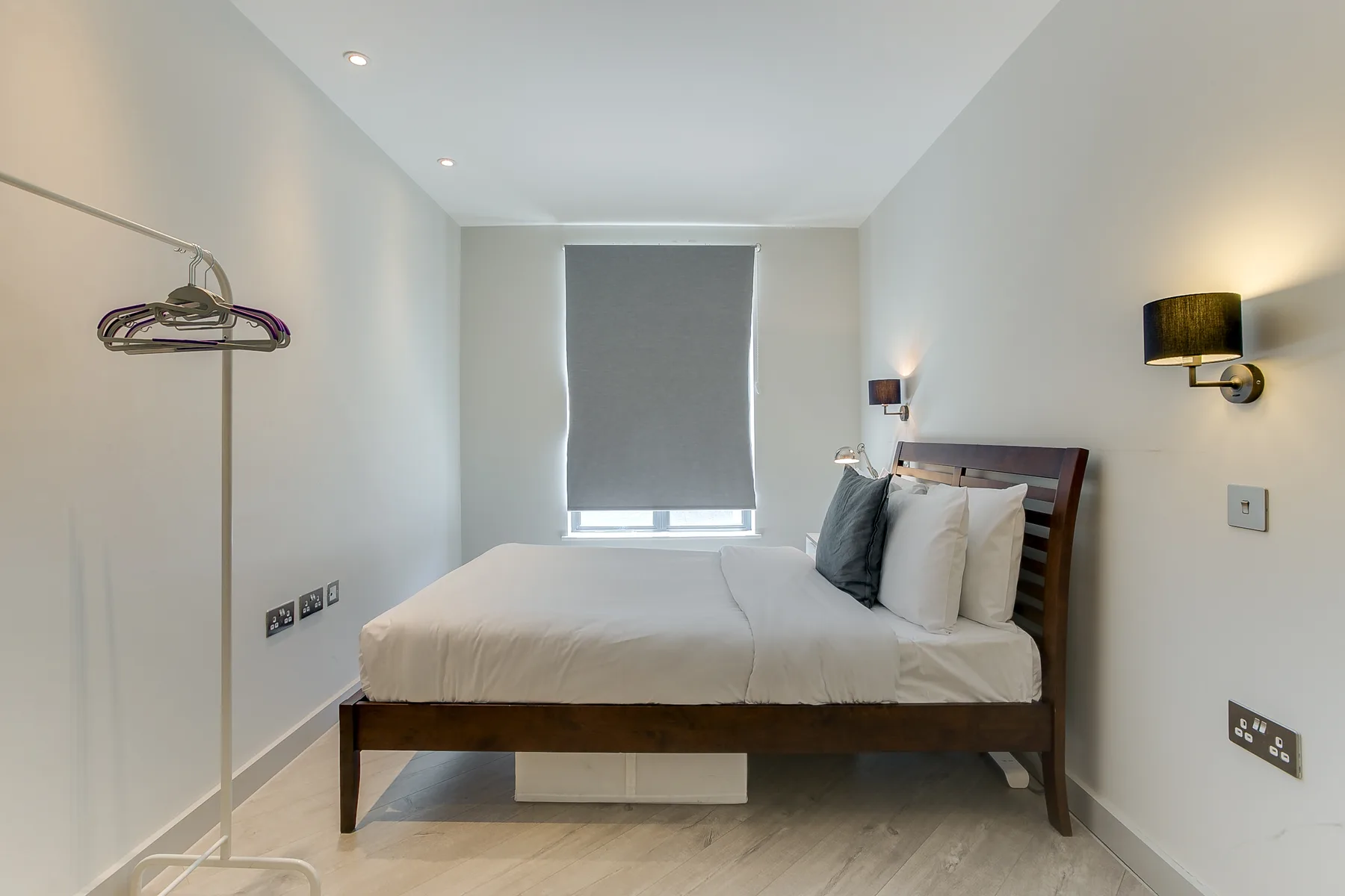 A bedroom with a neatly made bed and a gray window shade.