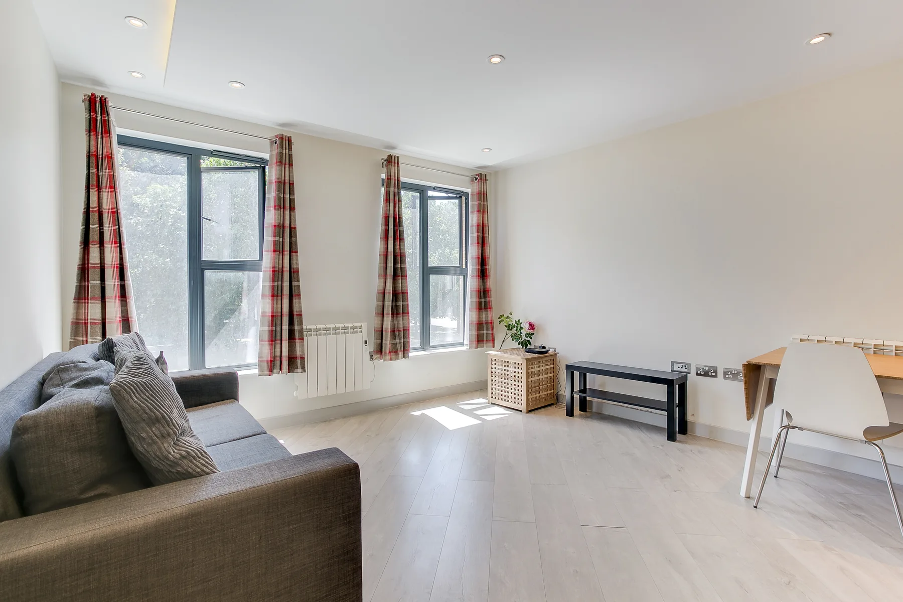 A bright living room with seating, tall windows, and plaid curtains.