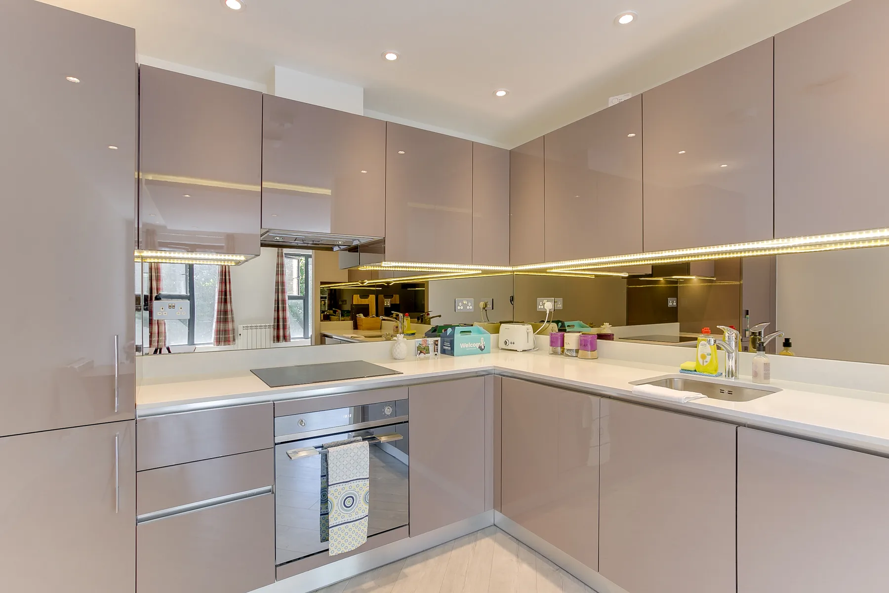 A modern kitchen with taupe cabinetry, white counters, and built-in appliances.