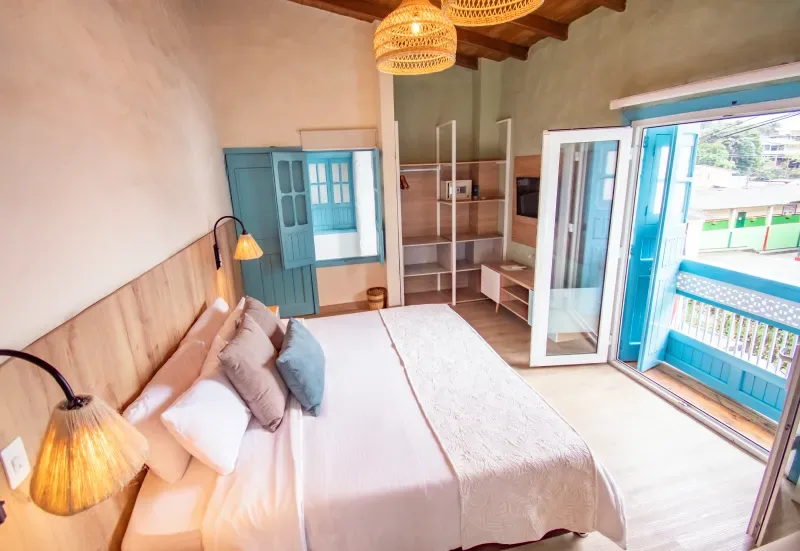 Habitación con cama, ventanas azules y muebles de madera clara.