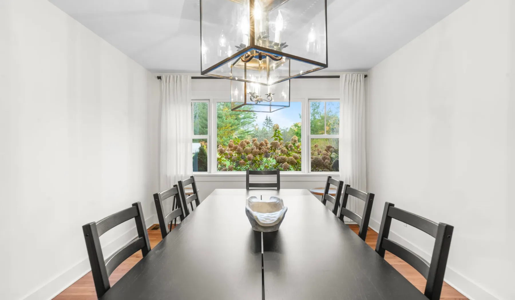 Comedor con una mesa larga, asientos oscuros y una ventana grande.