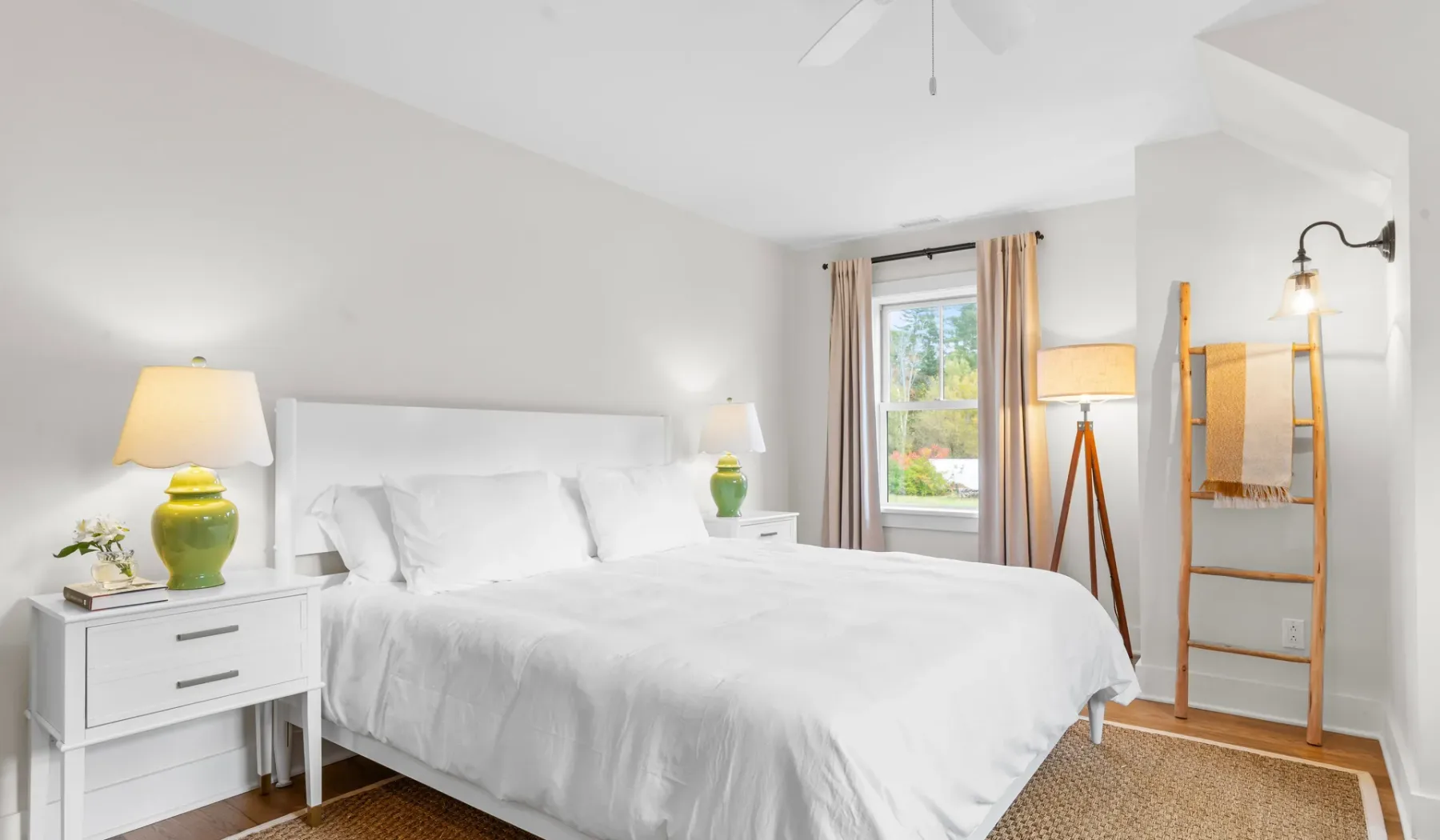 Un dormitorio luminoso con una cama blanca, mesitas de noche y una ventana.