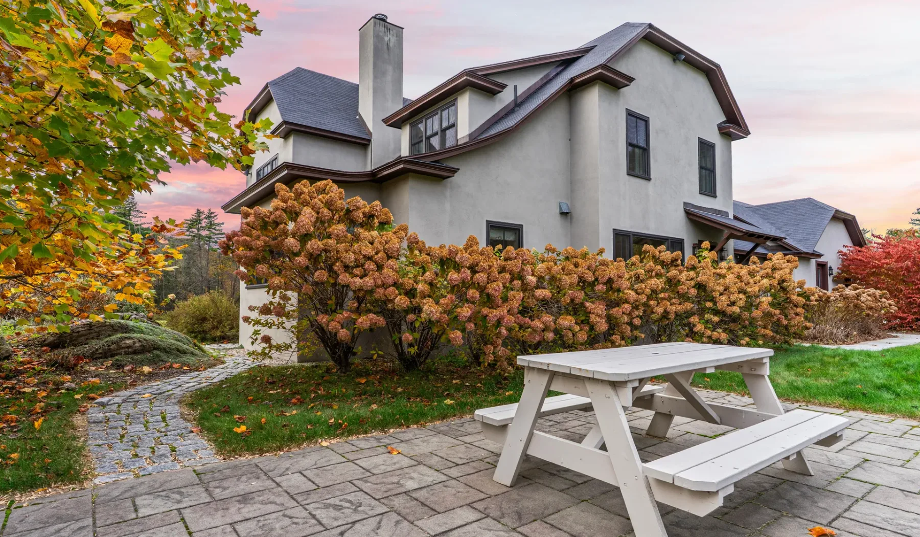 Una casa y una zona de patio con una mesa de picnic y arbustos.