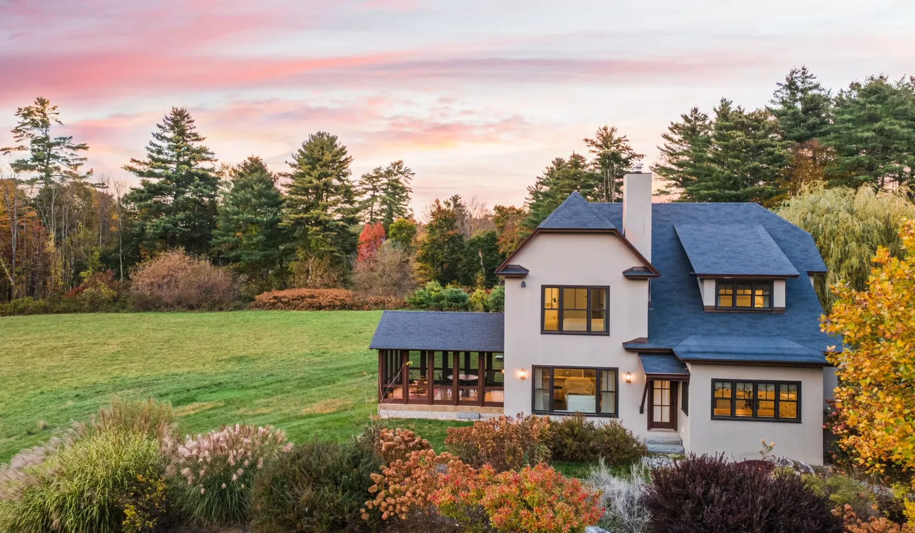 Una casa se encuentra junto a un césped y árboles bajo un cielo rosado al atardecer.
