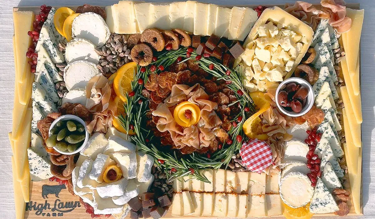 Una tabla de madera presenta una selección de quesos, carnes curadas, frutas y guarniciones.