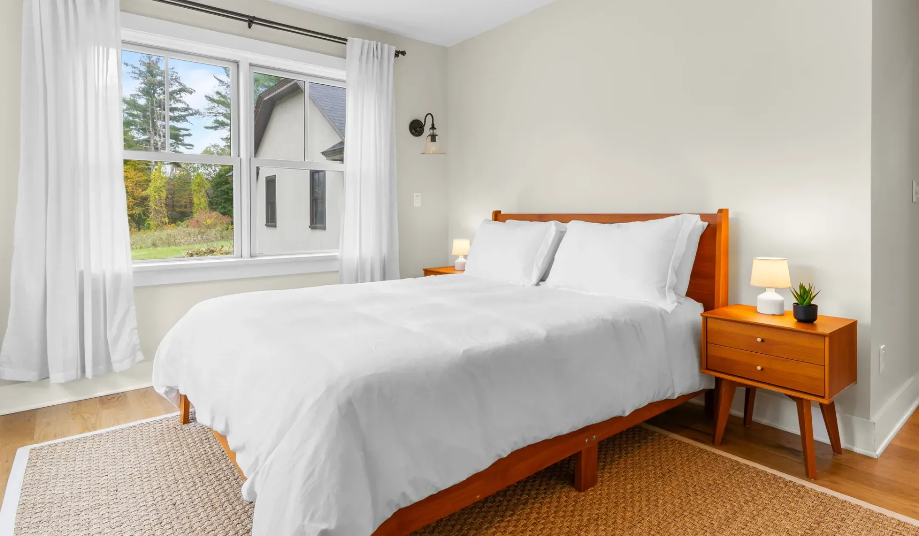 Un dormitorio luminoso con una cama blanca junto a una ventana grande.