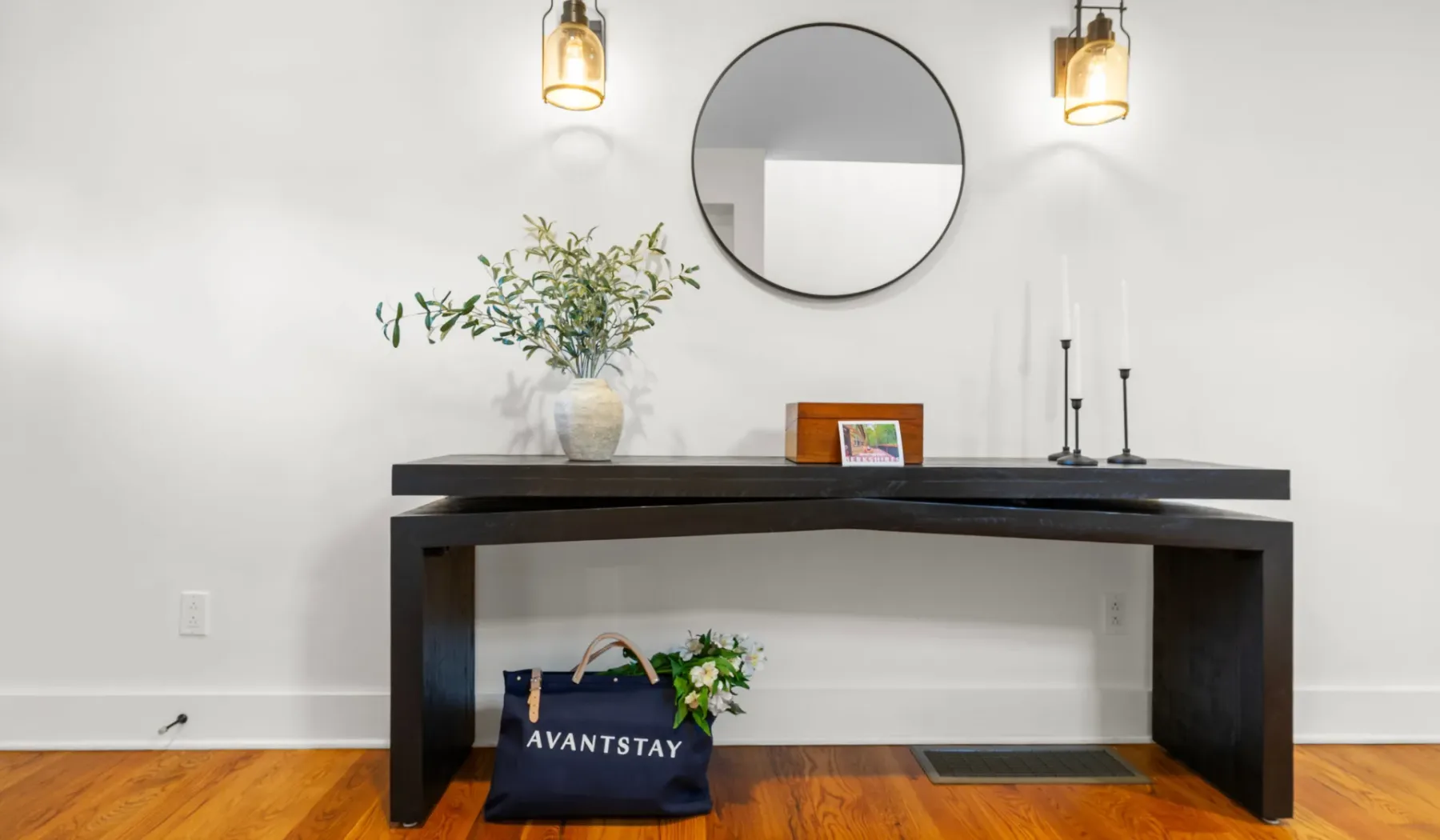 Una mesa consola oscura con objetos decorativos está junto a una pared blanca.